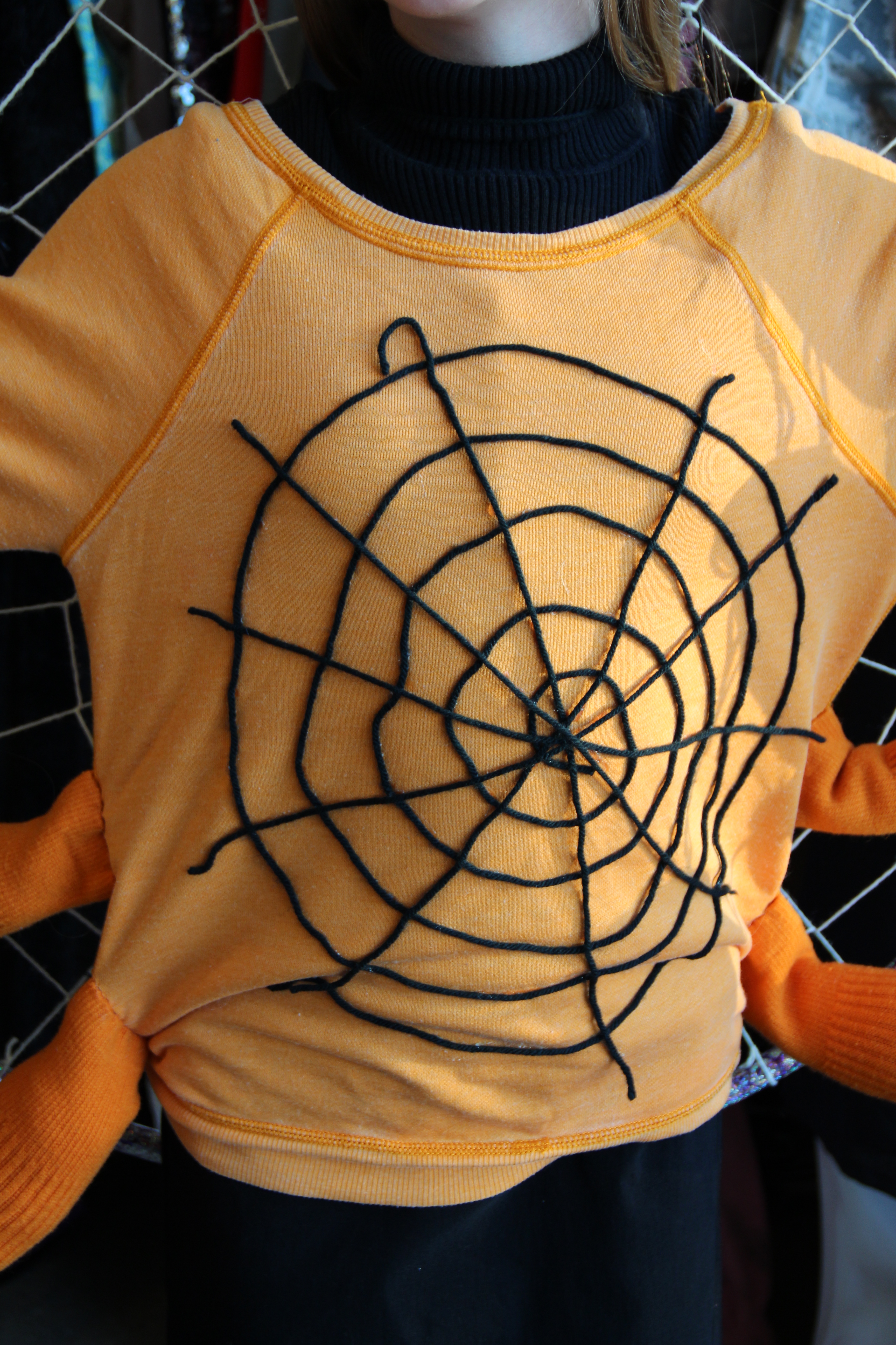 Lay additional yarn on the front of the sweat shirt in a spider web design. Hold in place with craft glue.